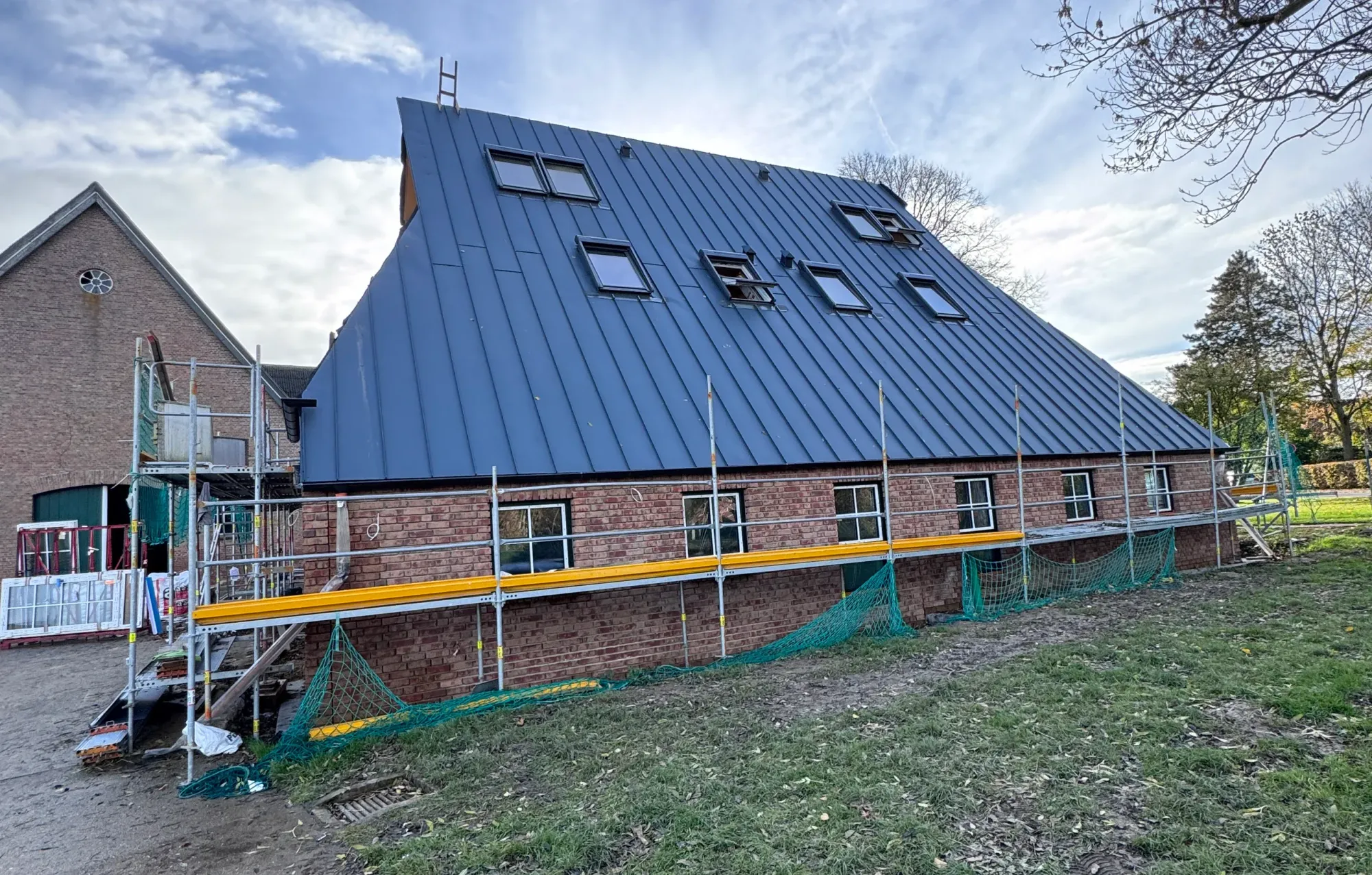 Scheune während des Umbaus mit neuem dunklem Stehfalz-Metalldach und Dachfenstern, eingerüstet